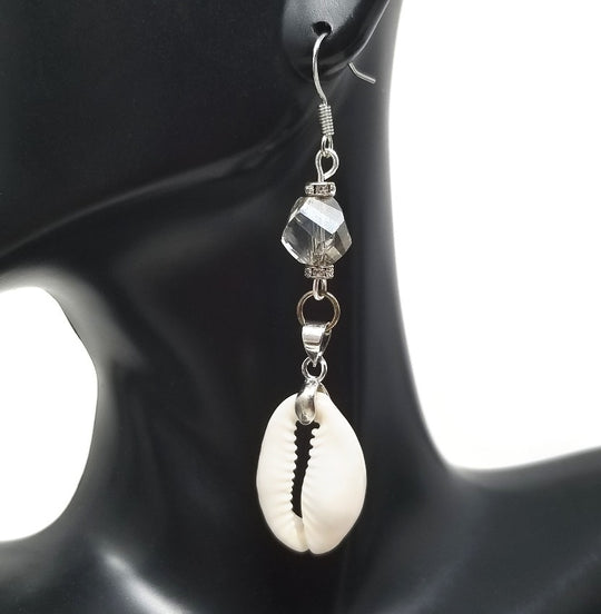 A pair of silver cowrie shell earrings with gray faceted glass beads, displayed on a mannequin head.